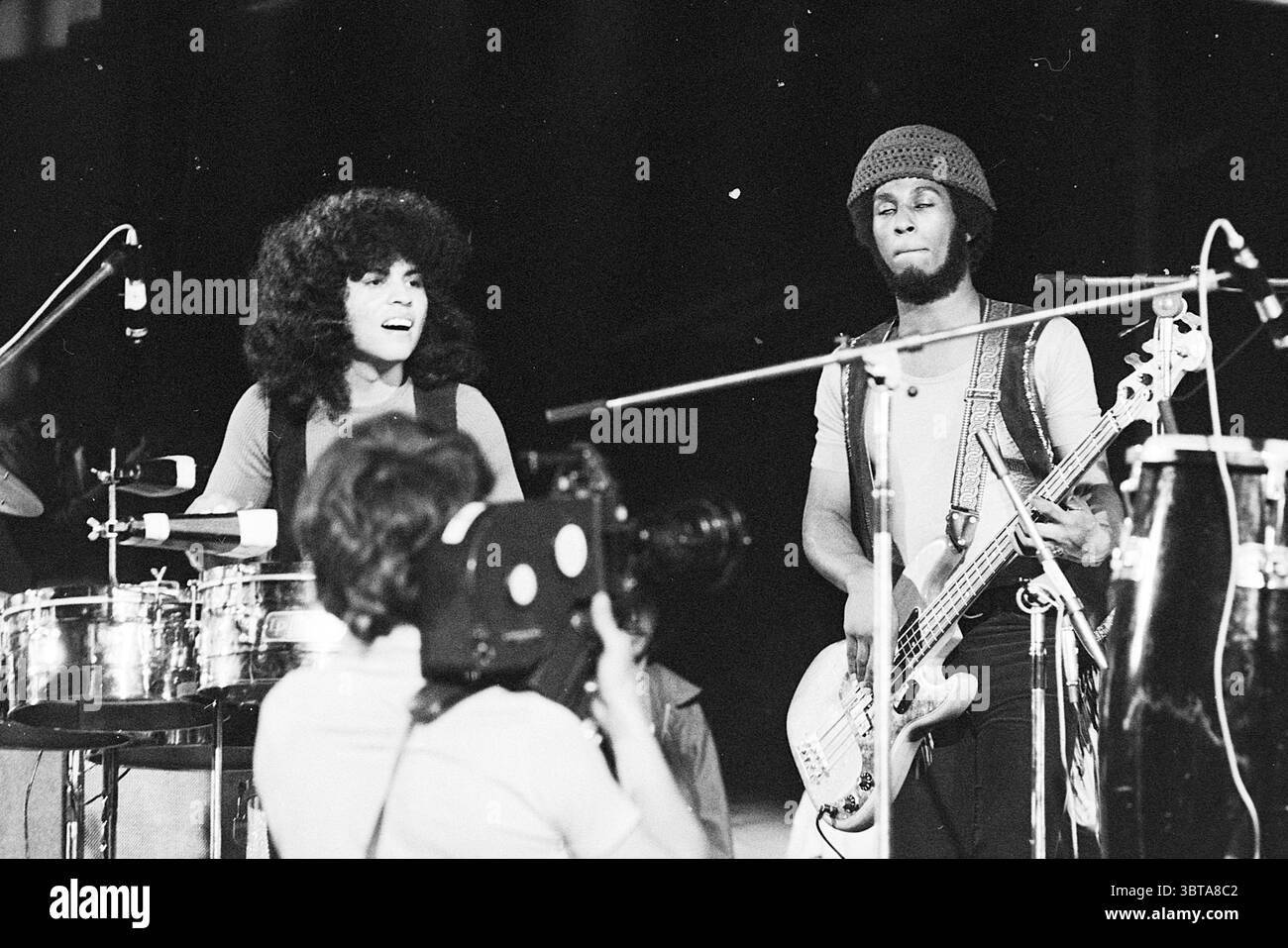 Holland Pop Festival in the Kralingse bos which has gone down in history as the Dutch version of the American Woodstock festival. With performances by The Byrds Mungo Jerry Canned Heat and Jefferson Airplane Music Rotterdam, Whizgle News, Dutch Desk, The Netherlands, 1950 - 2000 on 26-06-1970. The image includes these topics. The scene captures a lively musical performance, exuding a vibrant energy. To the left, a female percussionist plays a set of conga drums, her curly, voluminous hair framing her face, which beams with enthusiasm. She wears a sleeveless, dark top that contrasts with her ra Stock Photo