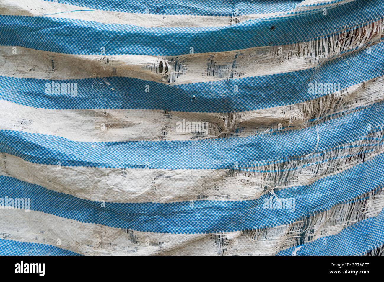 An old, tattered blue construction site tarpaulin Stock Photo