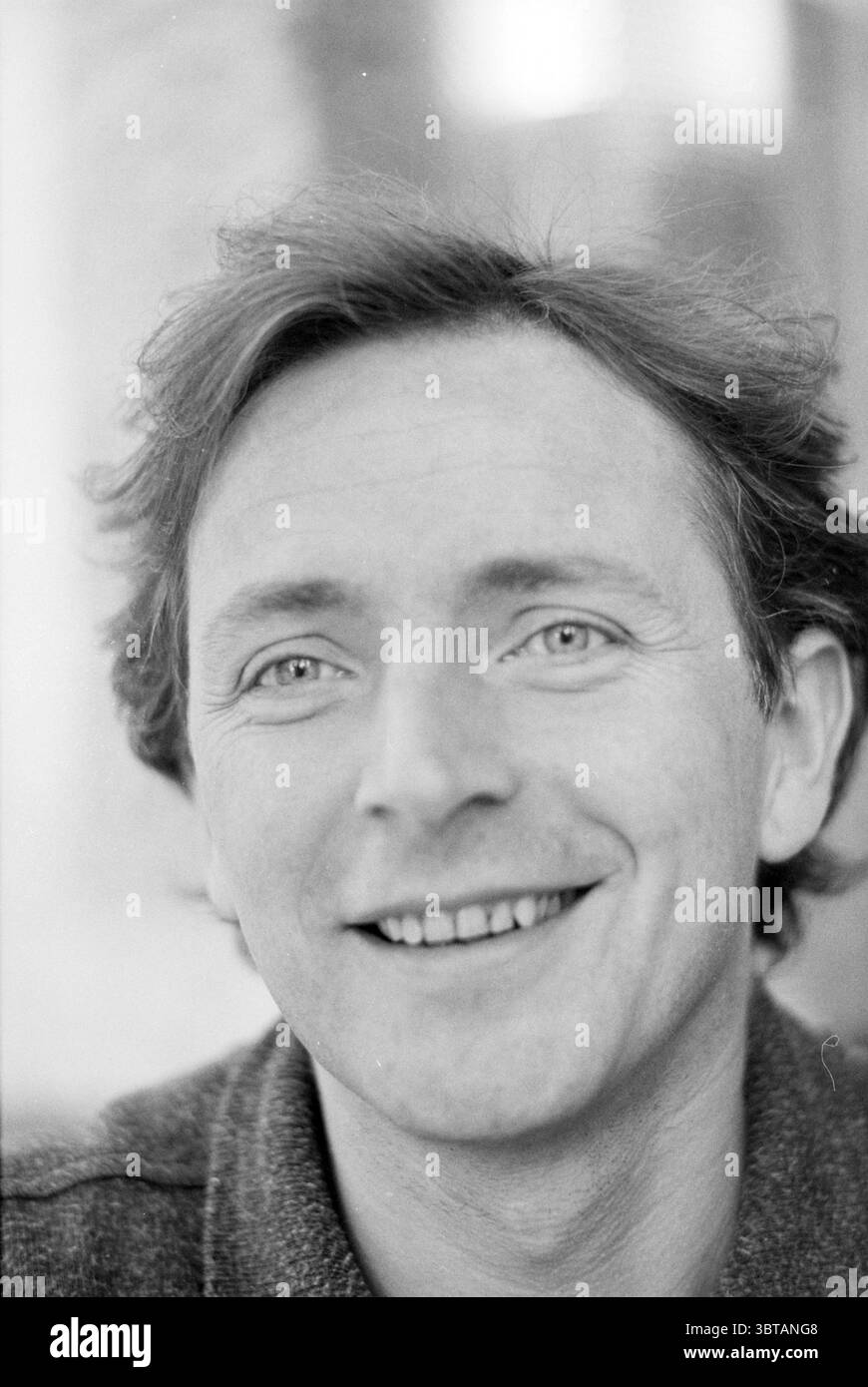 M. Verhegge theater technician, Whizgle News, Dutch Desk, The Netherlands, 1950 - 2000 on 27-11-1995. These topics appear in the image. The scene captures a man with a warm and inviting expression, characterized by a gentle smile that conveys a sense of friendliness. His hair is slightly tousled and has a natural, uncombed look, with soft waves that frame his face. The eyes are bright and engaging, reflecting a sense of curiosity and warmth, hinting at a lively personality. The background is softly blurred, creating a shallow depth of field that draws attention to the subject's face. The light Stock Photo