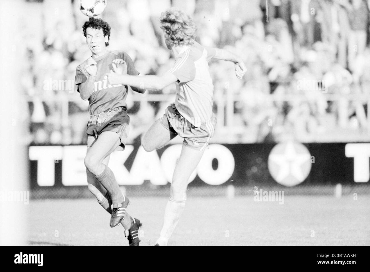 Haarlem - Fortuna Sittard Football Haarlem, Whizgle News, Dutch Desk, The Netherlands, 1950 - 2000 on 20-10-1985. The image shows these topics. In the scene, two players are intensely engaged in a soccer match. One player, wearing a dark jersey with white accents, appears to be mid-movement, possibly attempting to evade the other. The second player is dressed in a lighter, more muted uniform, hinting at vintage sports attire. The action captures the moment just before the lighter-dressed player skillfully kicks the ball, which hovers in the air, creating a sense of motion. The expressions on b Stock Photo