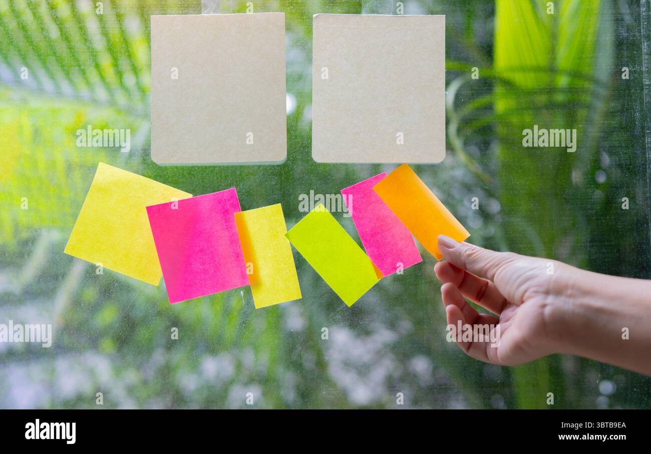 Close-up people holding paper post it in hand on glass wall board. Empty space for text. Stock Photo