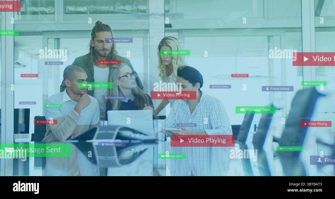 Collaborating five professionals showing software features in glass office, with laptops and tablet Stock Photo