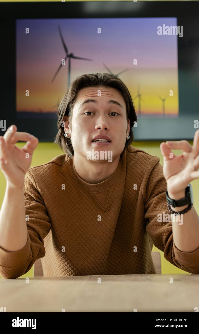 Asian man making OK gestures sitting at wooden table in room with wind ...