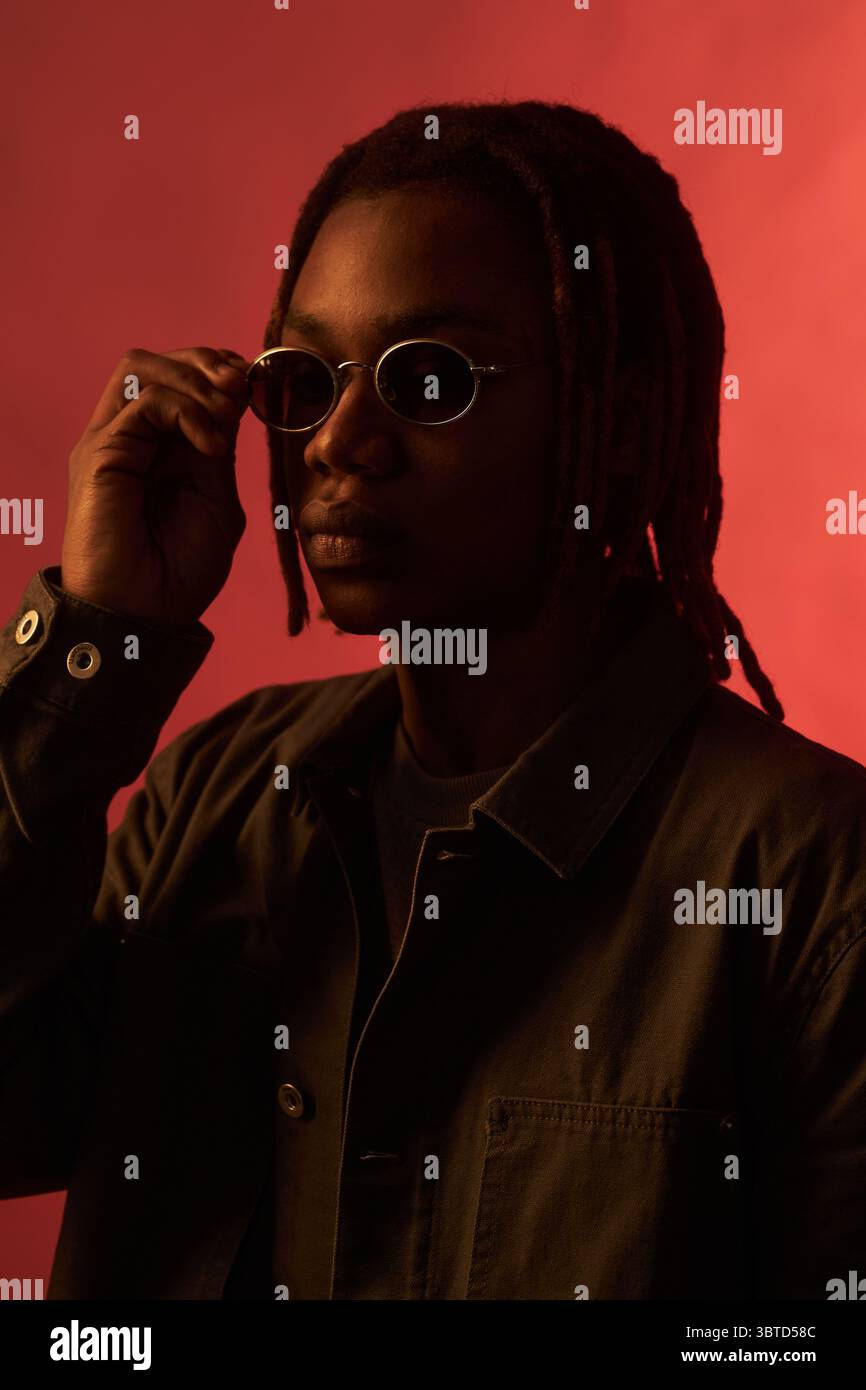 Young adult Black man adjusting sunglasses while facing camera, wearing ...