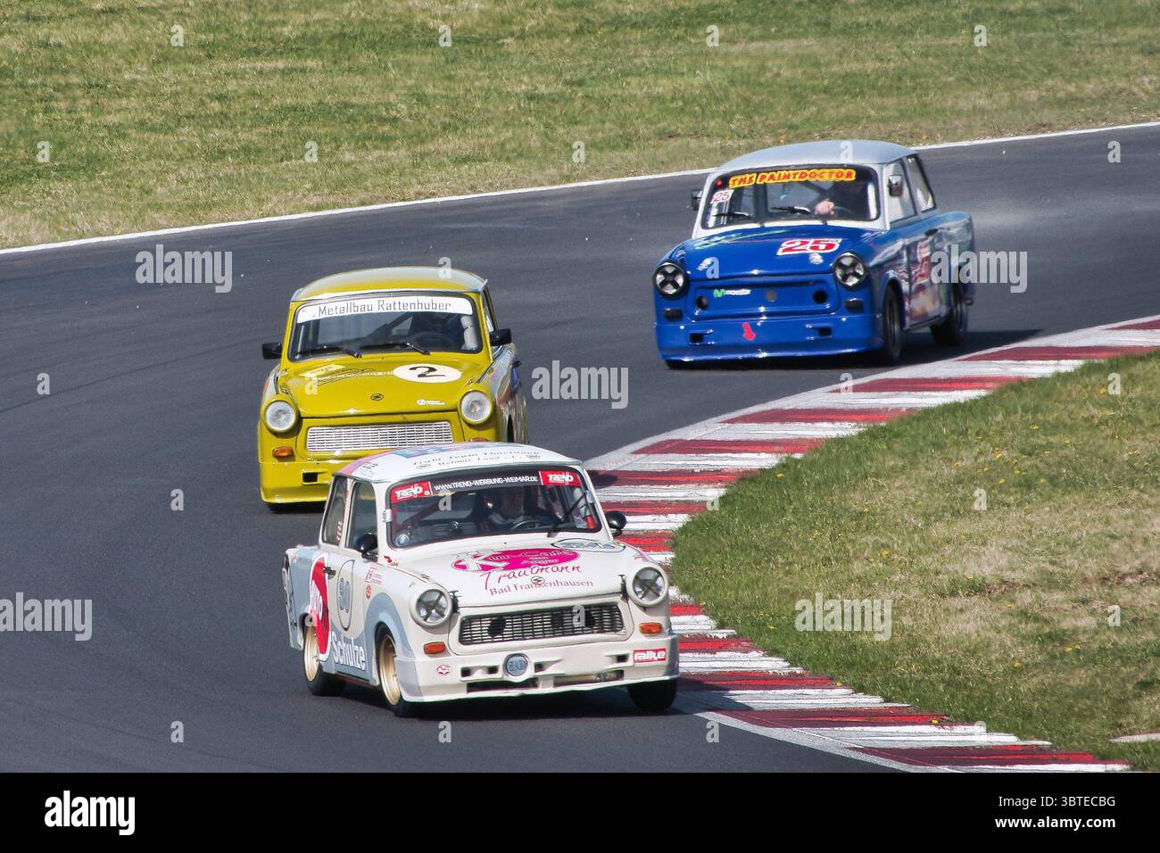 Three Trabant 601 cars competing in historic motorsport on the Most Circuit (Czech Republic). A white, a yellow, and a blue Trabant are racing through Stock Photo