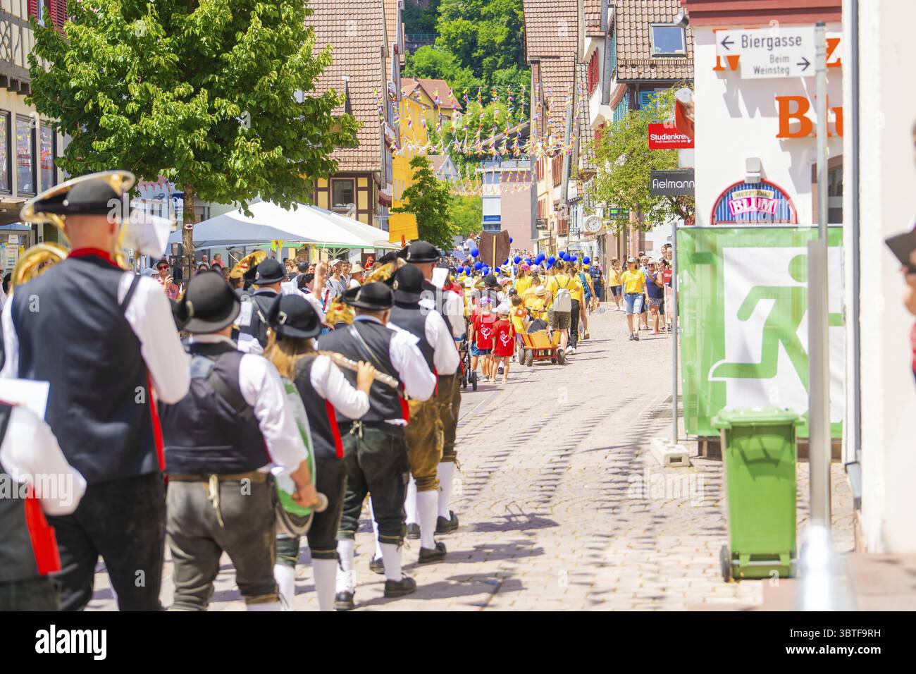 People in traditional costumes march in a sunny village street during a ...