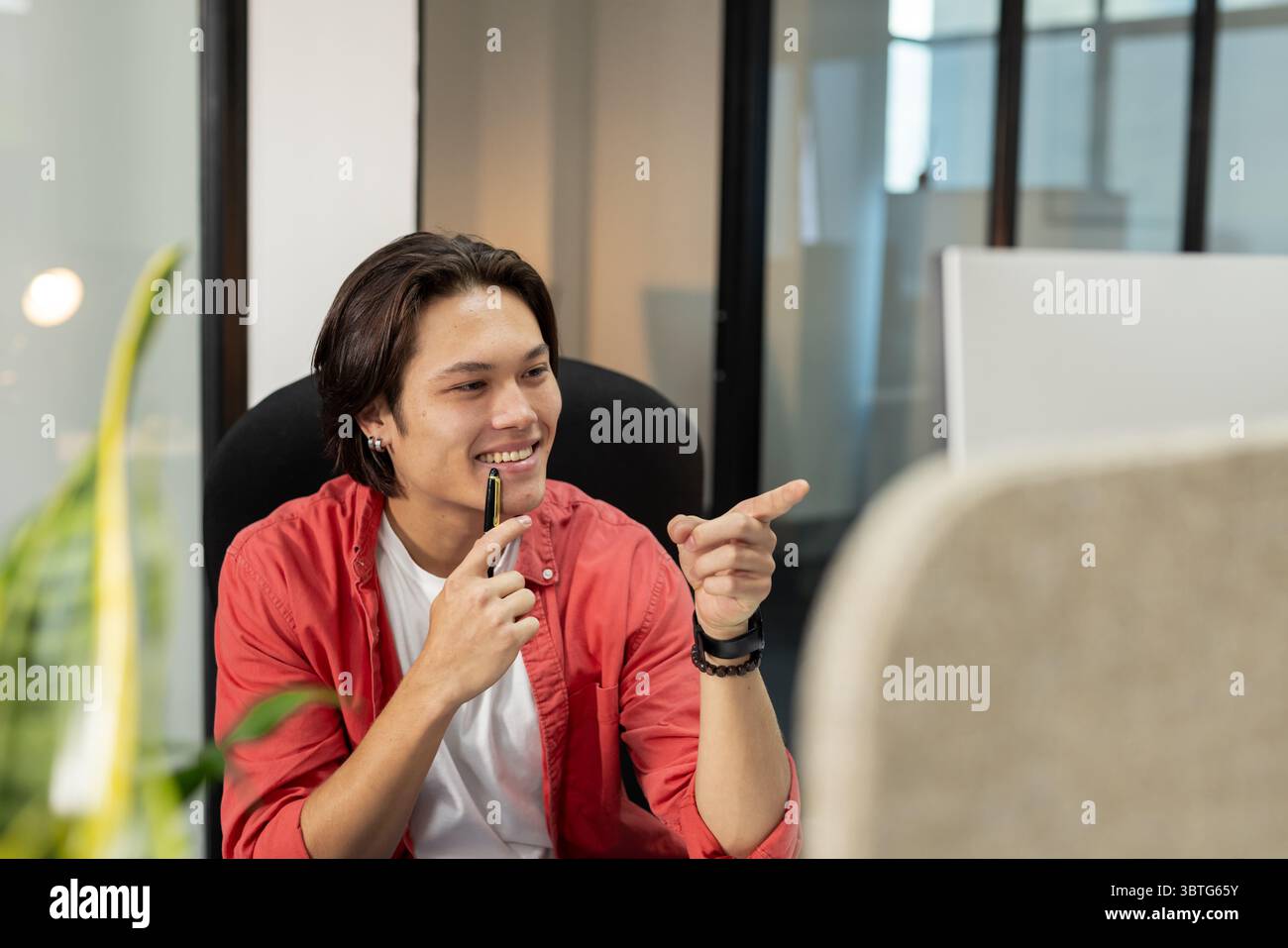 Asian man sitting in office chair at desk holding pen and pointing ...
