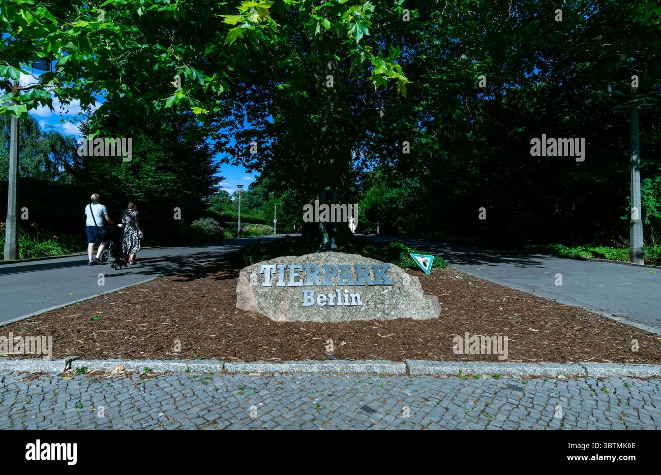 Entrance Sign at Tierpark Berlin Zoo with Visitors Passing. A large granite stone featuring the name "Tierpark Berlin" at the zoos main entrance. Stock Photo