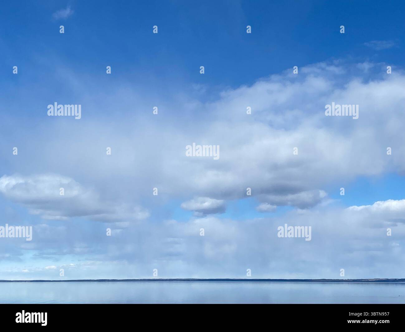 The vast blue sky is filled with soft white clouds, reflected in the calm water below. - Smartphone Captured Stock Image