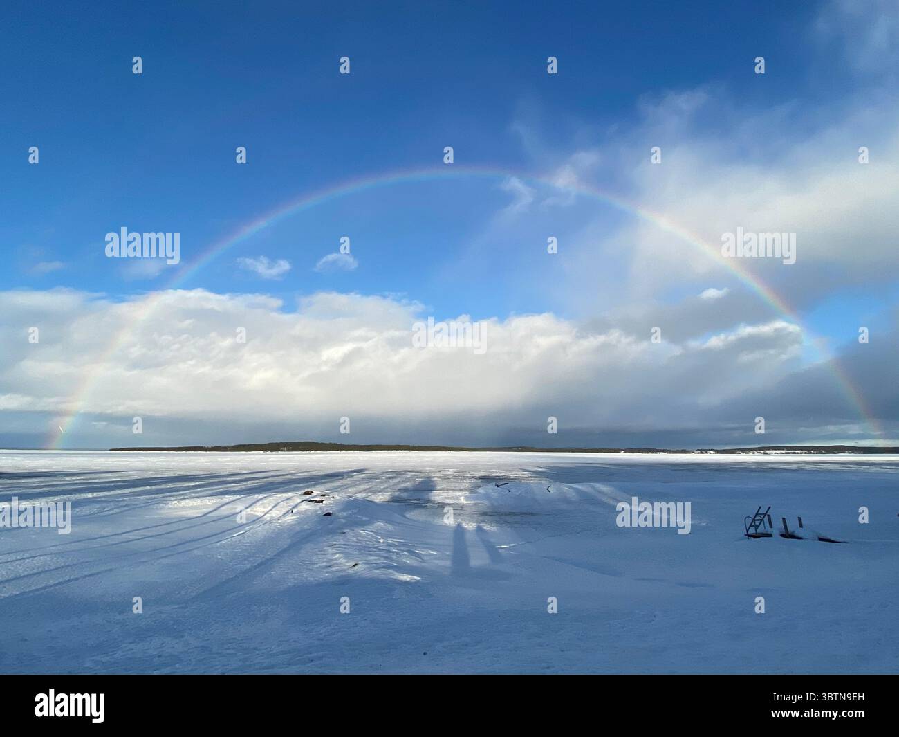 A stunning rainbow appears over a snow-covered field on a bright winter day. - Smartphone Captured Stock Image