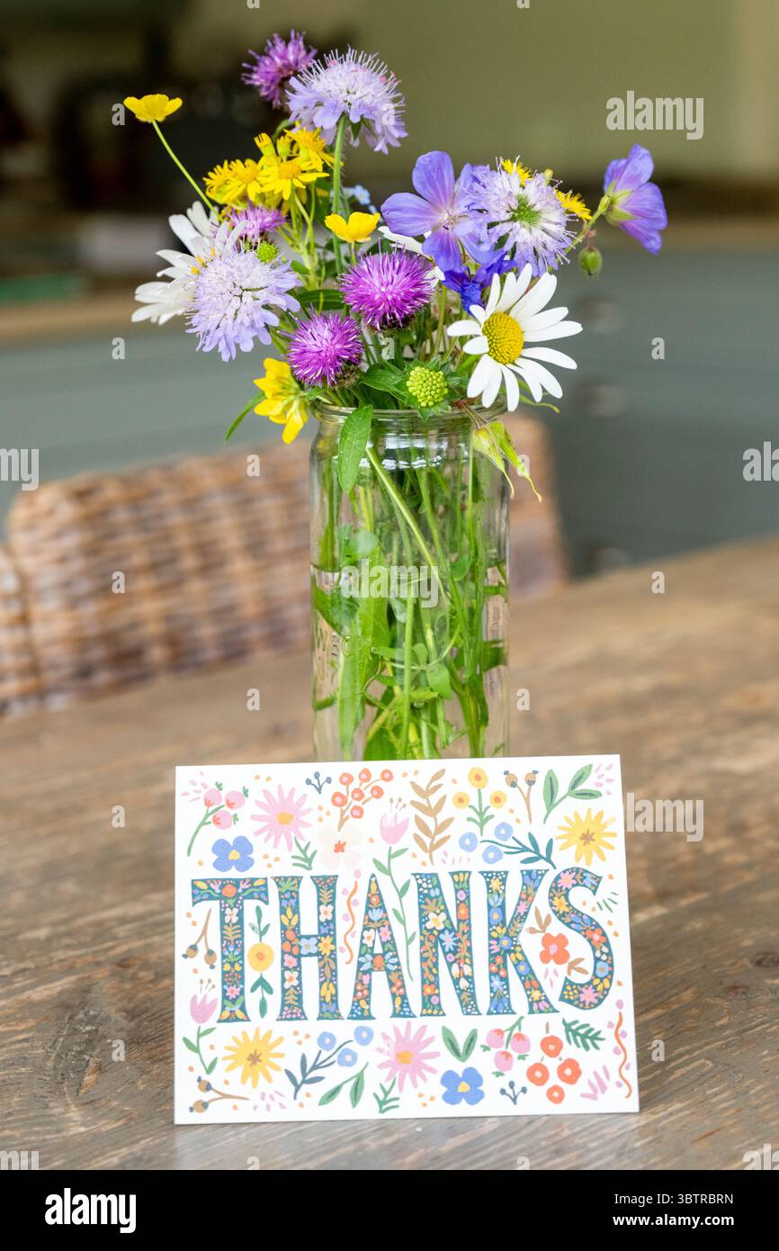 Hand picked bouquet of garden flowers - ox eye daisy, buttercups, geraniums, scabiosa, knapweed, in glass vase with thank you card Stock Photo