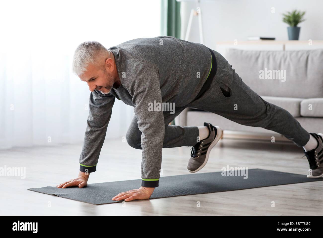 Athletic bearded senior man doing exercises at home Stock Photo