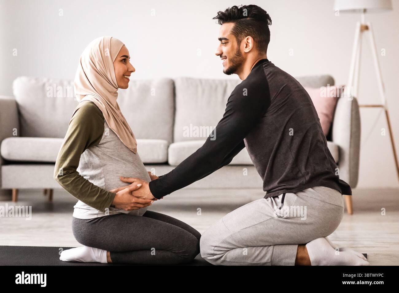 Pregnancy Workout. Happy Muslim Spouses Practicing Yoga Together At Home, Side View Stock Photo
