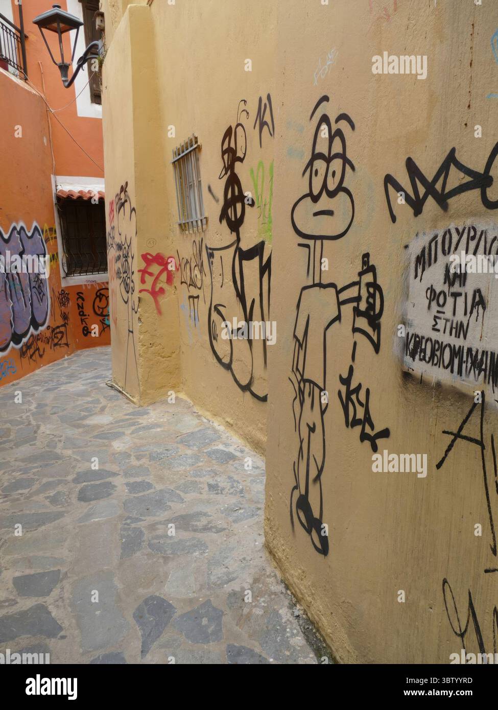 CHANIA, CRETE - MAY 5, 2025 - Cartoon graffiti character holding spray paint can decorating narrow alley walls in Athens Greece Stock Photo