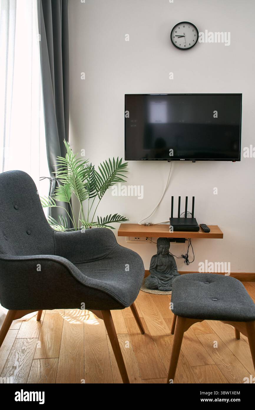 Modern living room featuring a grey armchair, wall-mounted tv, clock ...