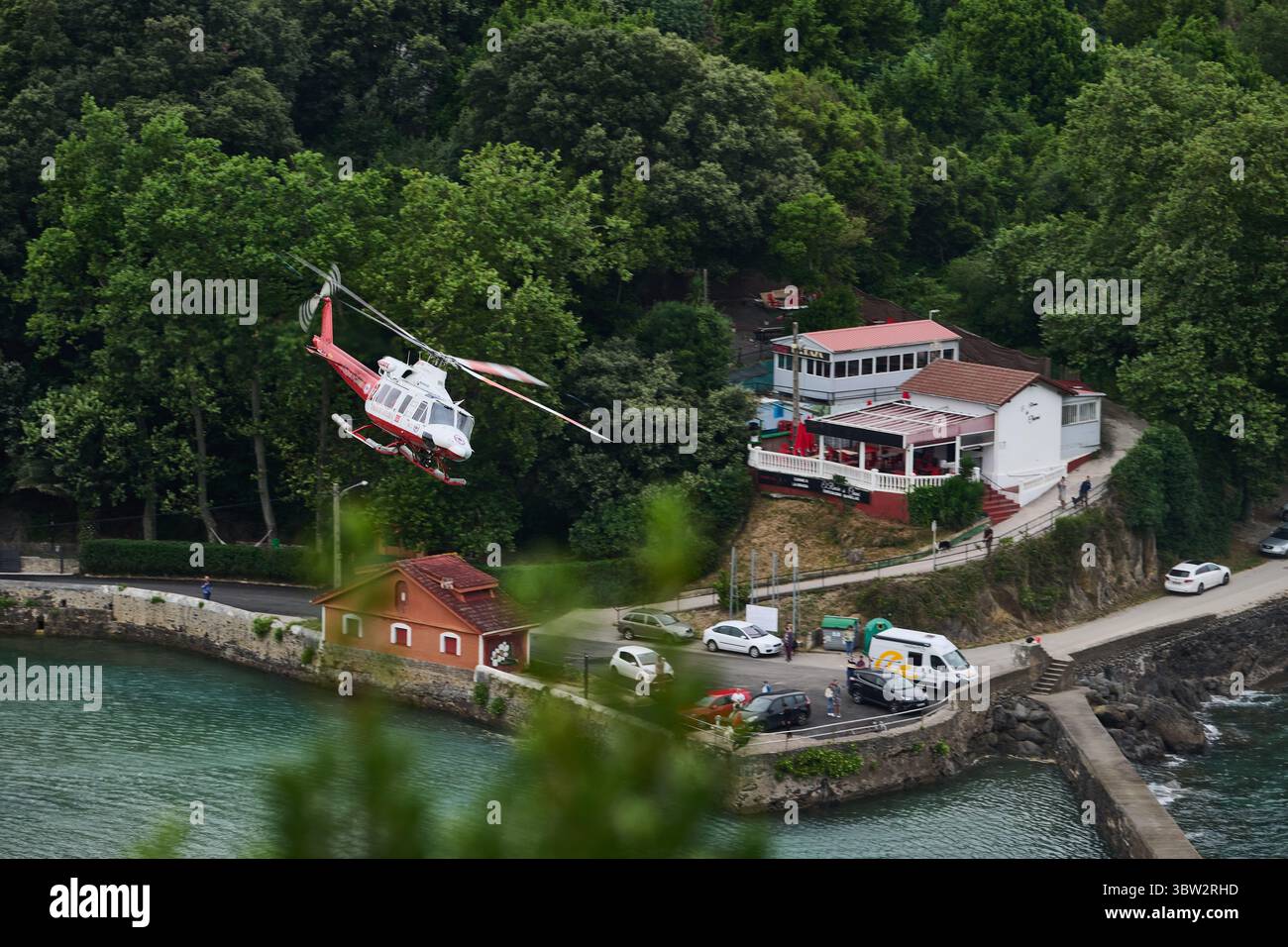 Red and white rescue helicopter flying over a coastal town in cantabria ...