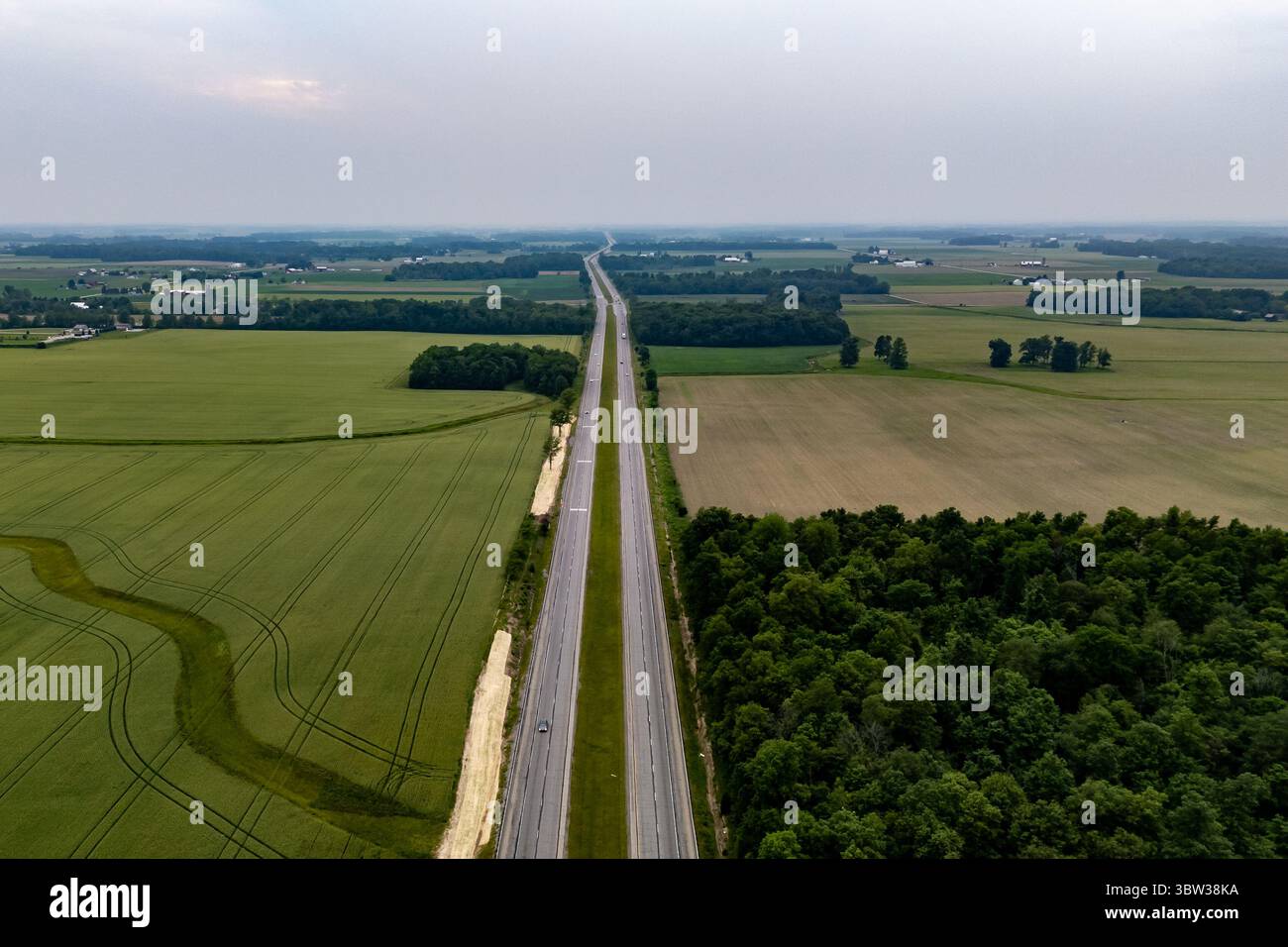 Lonely road cutting through vast field. Stock Photo