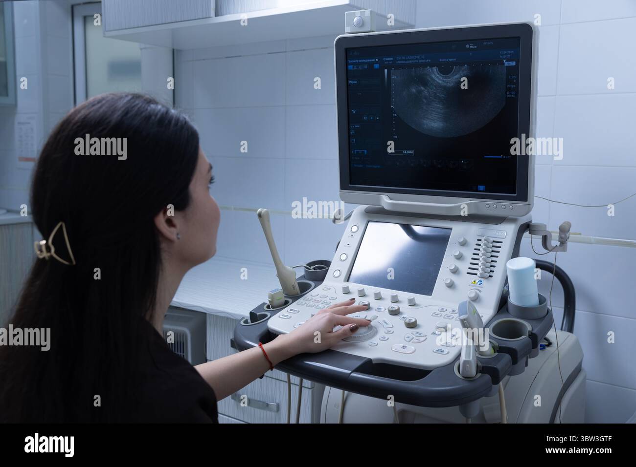 A Female Medical Professional Operating an Ultrasound Machine, Observing Diagnostic Images on the Monitor in a Well-Designed Clinical Environment Stock Photo