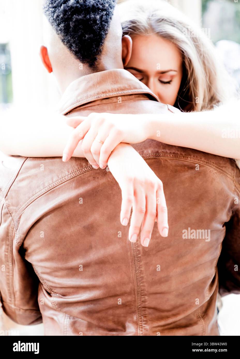 A woman embraces a man from behind, her arms wrapped around his chest ...