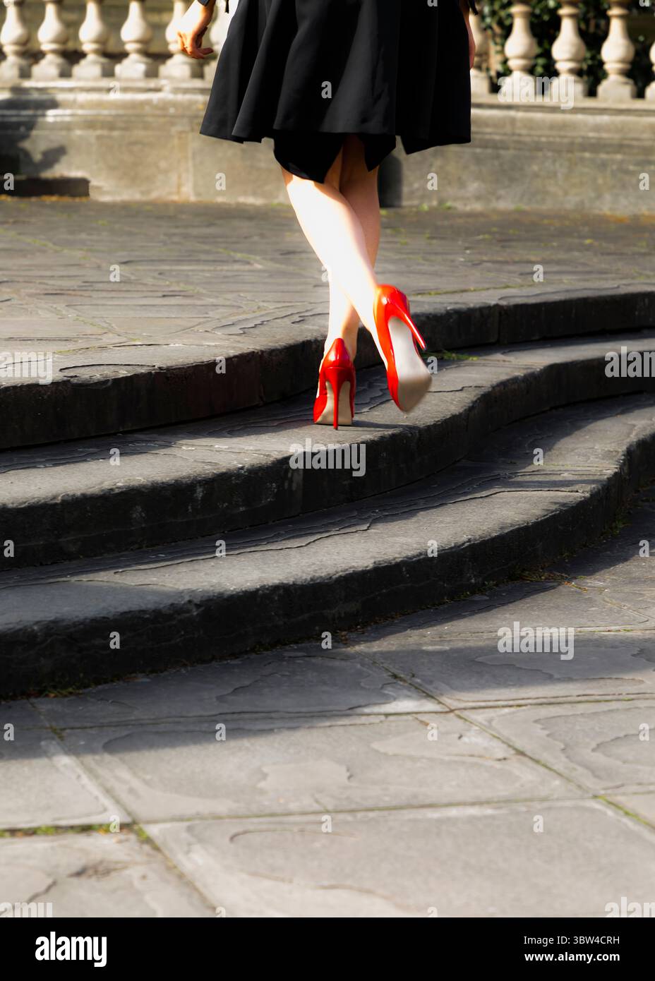 A person wearing red high heels walks up a set of stone steps. Stock Photo
