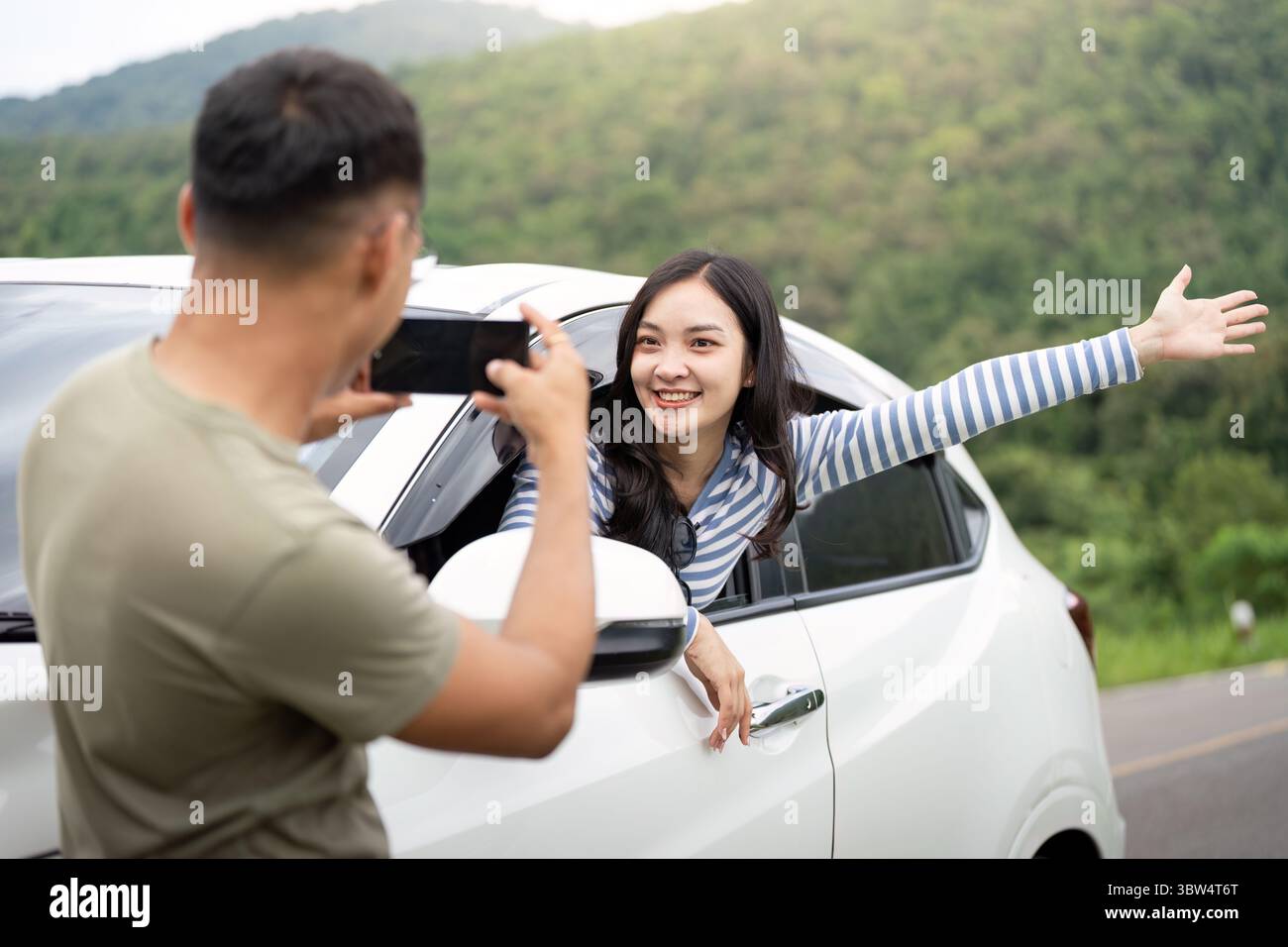 Joyful Adventure. Young woman enjoying a car ride while being photographed. Stock Photo