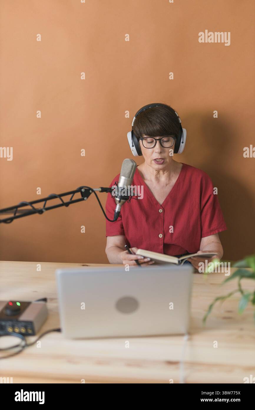 Portrait of mature woman wearing headphones and talking at online radio station - podcast and broadcast concept Stock Photo