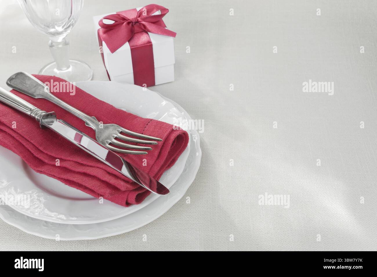 Beautiful decorated table with white plates, gift box with a red ribbon, cutlery and wine glass on tablecloths, with space for text Stock Photo
