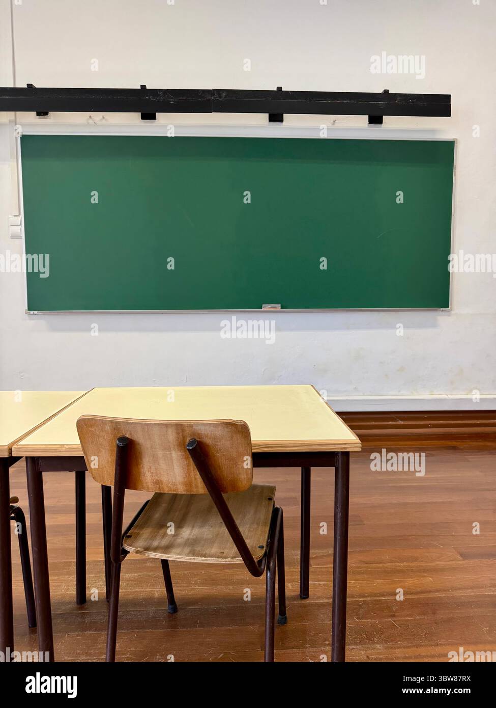 Empty classroom with a single student desk and a green chalkboard on the wall - Smartphone Captured Stock Image