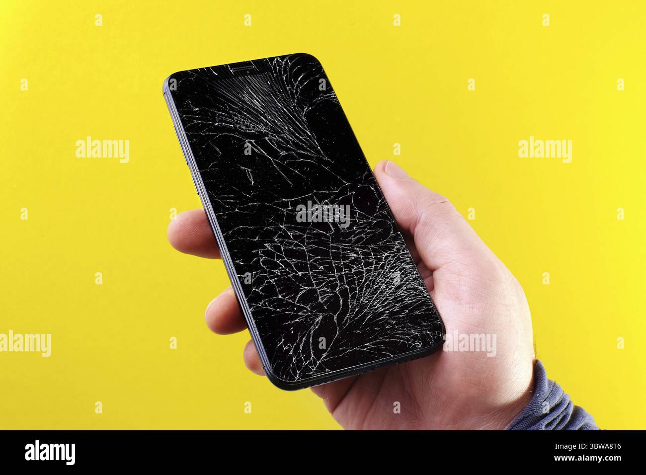 Black smartphone with a broken touch screen in hand on a yellow background. In a man's hand is a mobile device with cracked glass Stock Photo