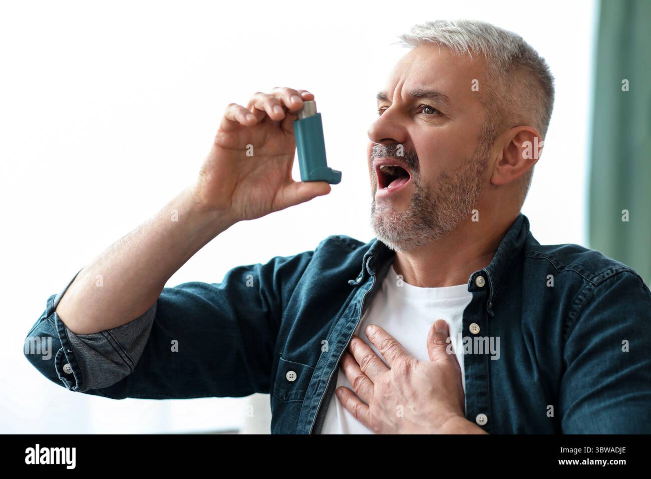 Senior man touching chest and using inhaler Stock Photo