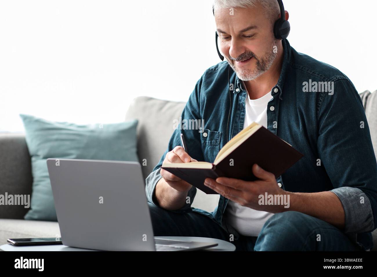 Happy old man having online class, using laptop and headset Stock Photo