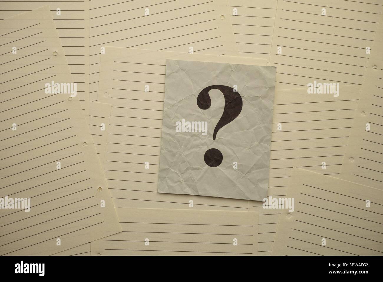 Crumpled gray paper note with question mark on it lying on lined notebook pages. Stock Photo