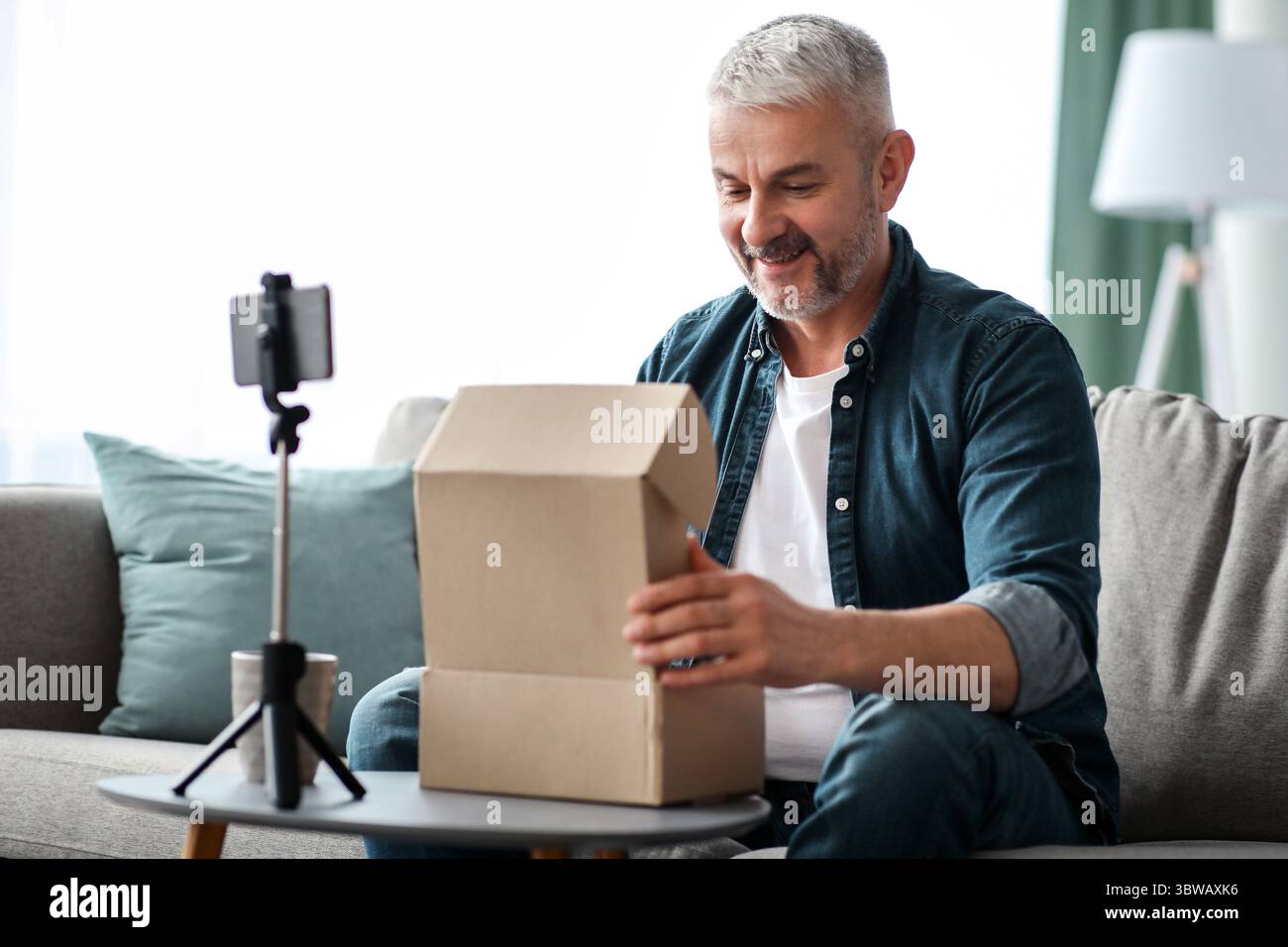 Happy senior man blogger broadcasting while opening delivery box Stock Photo
