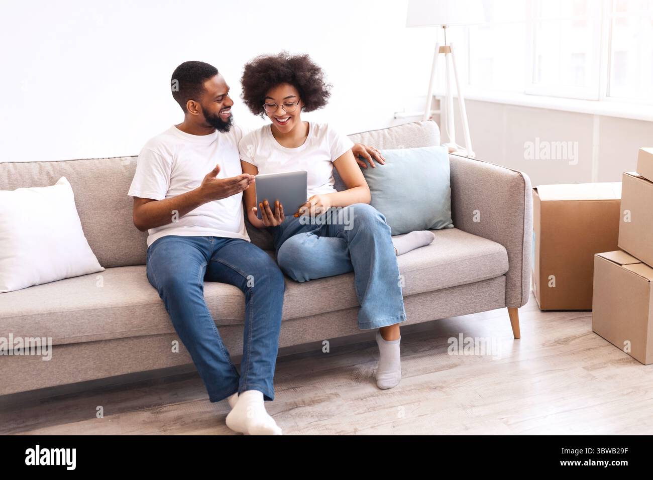 Happy Black Spouses Using Tablet Sitting Among Moving Boxes Indoor Stock Photo