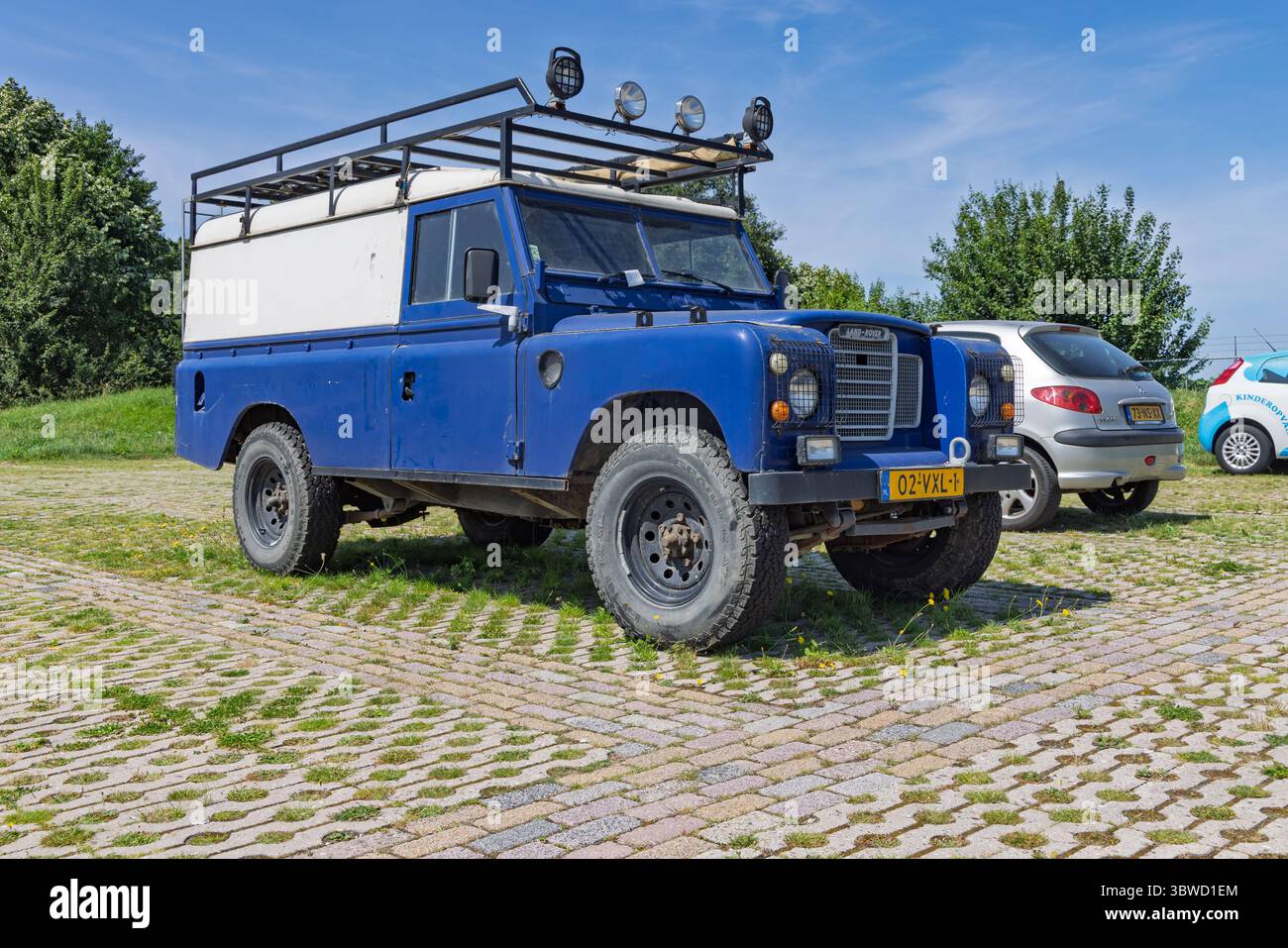 A classic blue Land Rover Series 3 with a roof rack parked on a paved ...