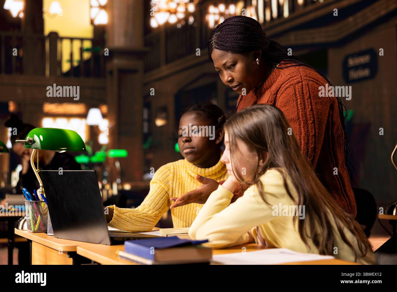 African american professor providing instruction to diverse girls during a private learning session, assisting with homework and school projects in a library. Doing tutoring activity for guidance. Stock Photo