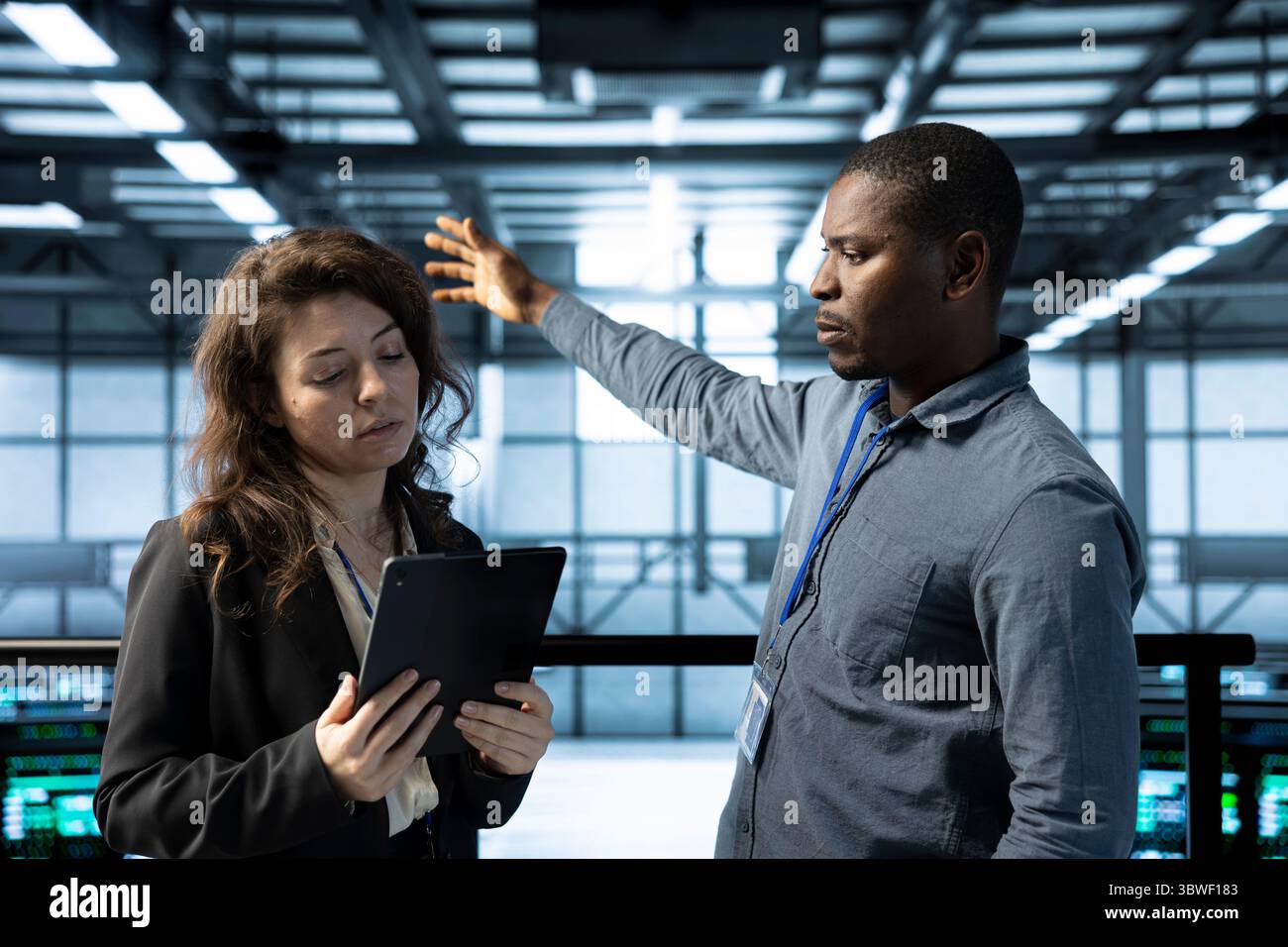 Teamworking admins in data center automating routine maintenance tasks with tablet, executing diagnostic scripts. Server farm colleagues using device, adjusting cooling and power settings Stock Photo