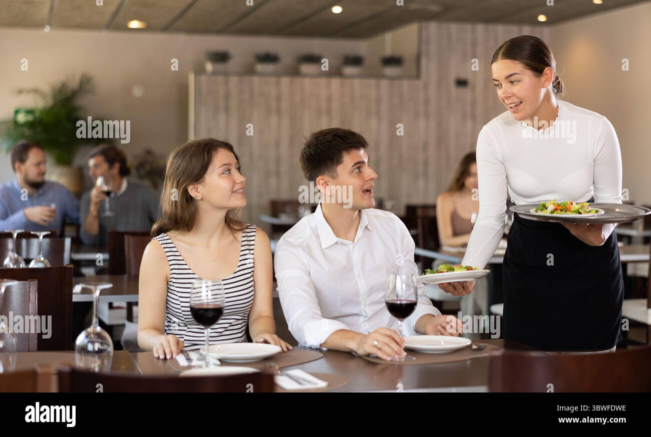 Waitressing Man Waitress brings order to young man and woman couple Stock Photo - Alamy