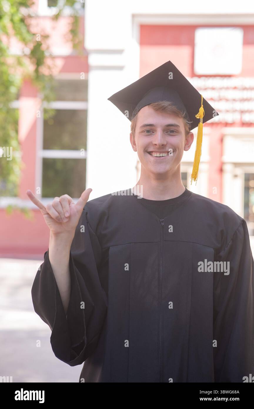 Caucasian young man in graduation gown communicating using sign ...