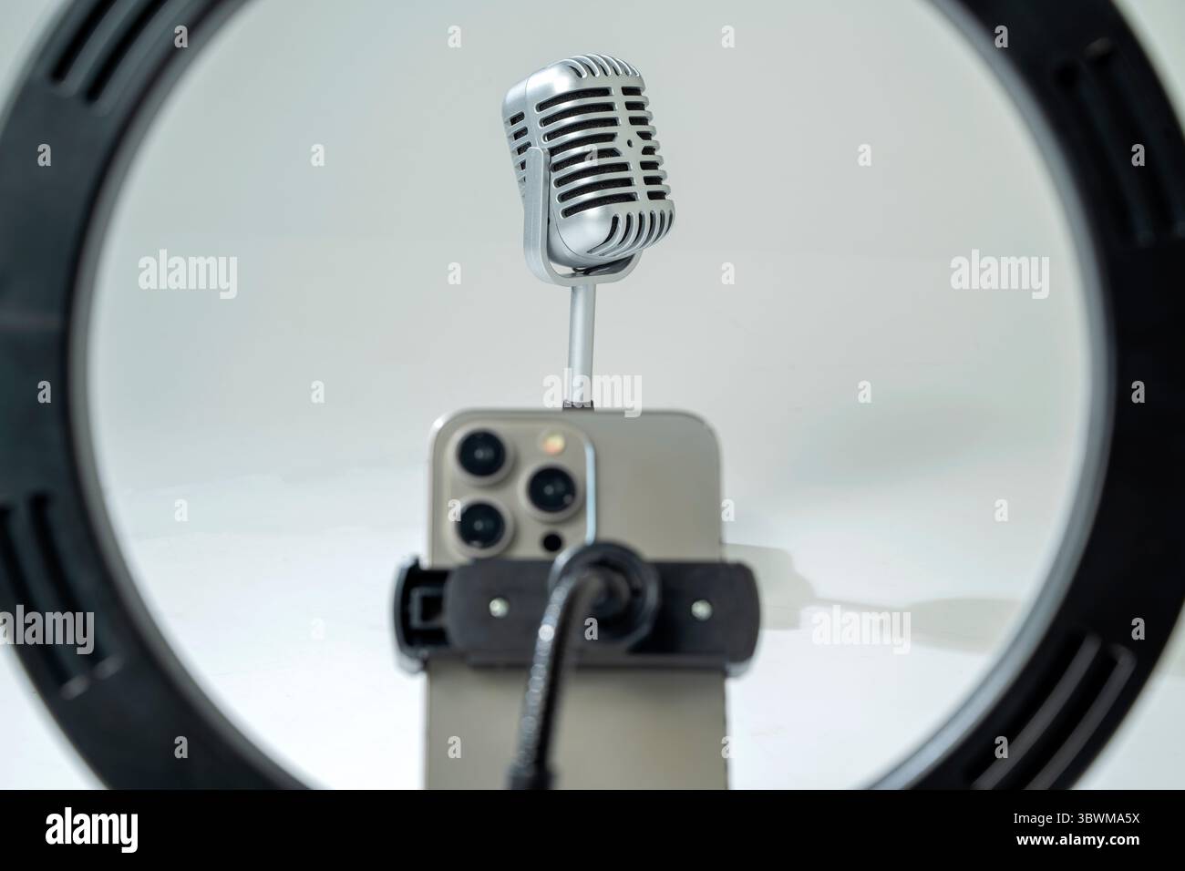 Round LED ring light with a cellphone on a phone holder with a vintage silver microphone with a white background. Vlogging or live streaming equipment Stock Photo