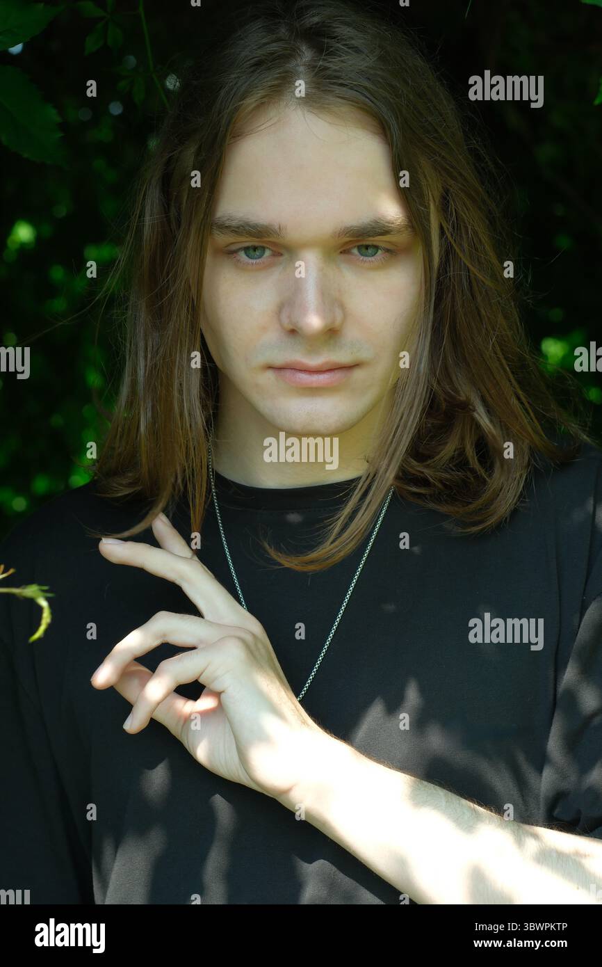 A young man stands confidently in a verdant setting, with a serene expression. Stock Photo