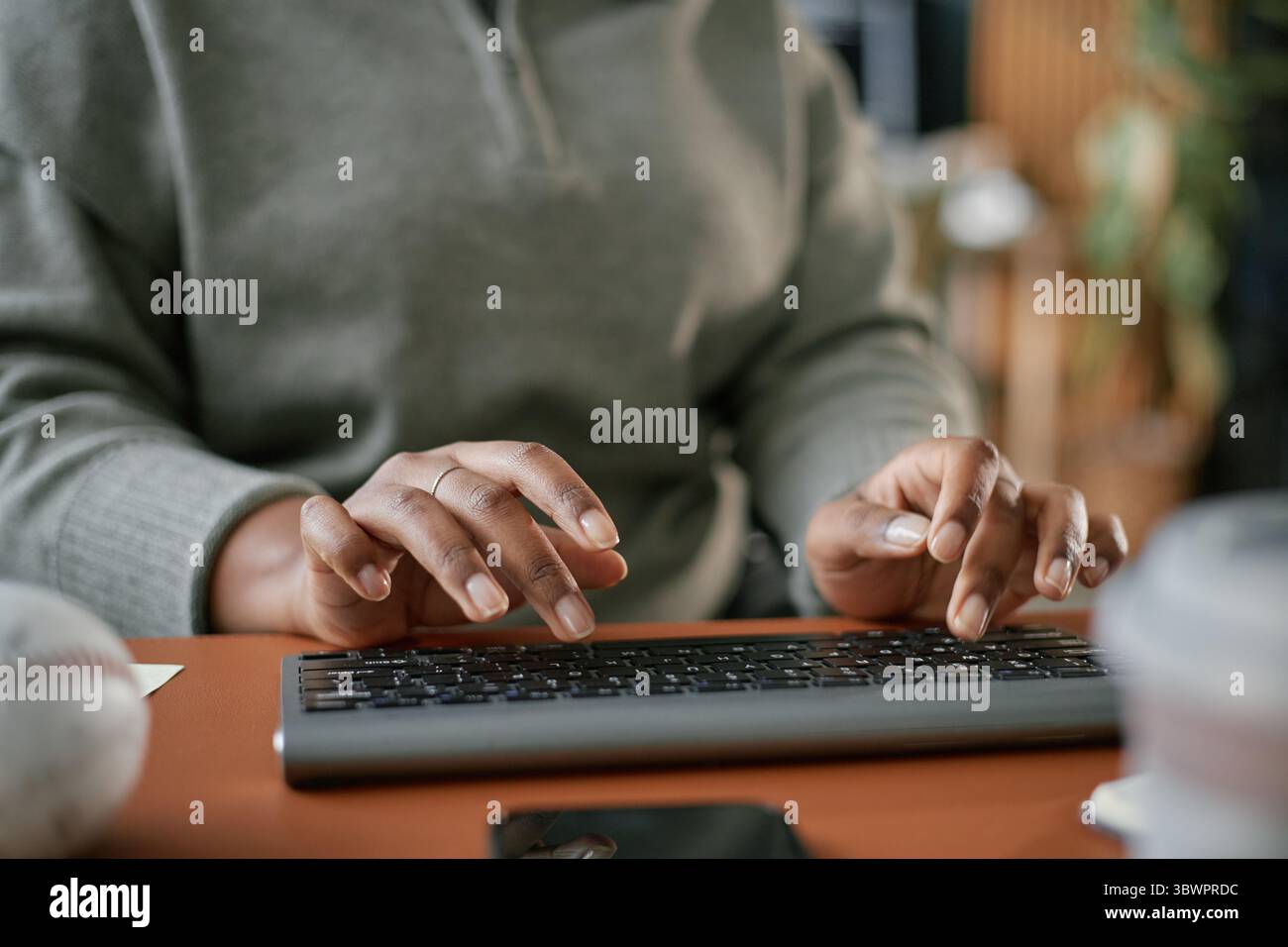 Black woman typing on wireless keyboard at desk, hands in focus ...
