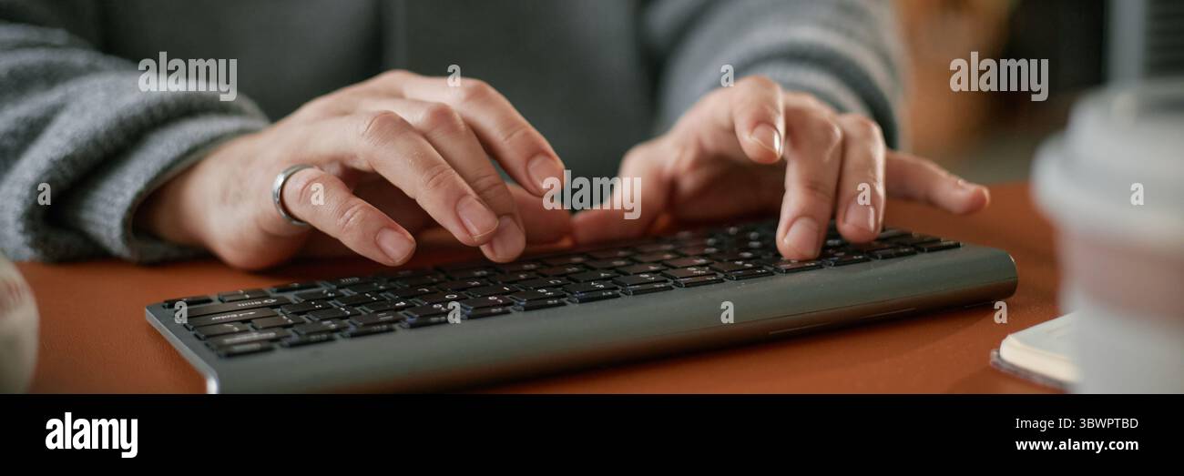 Website header shot of Caucasian middle aged man typing on wireless keyboard with both hands, wearing ring, focusing on work task, close up of hands and keyboard on desk Stock Photo