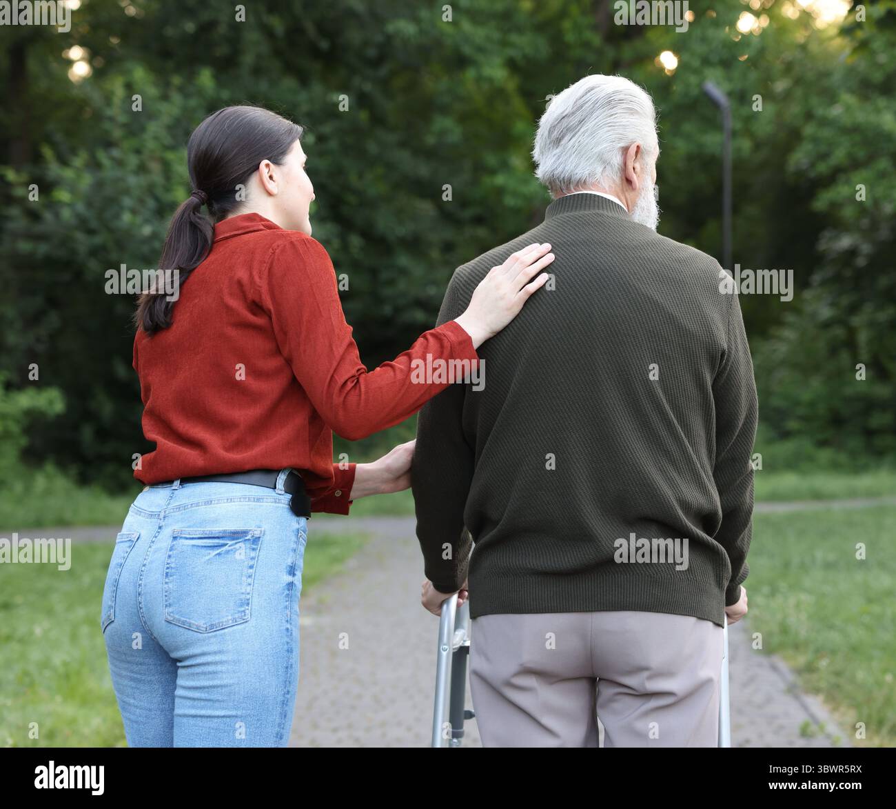 Caregiver supporting elderly man who using walking frame outdoors, back ...