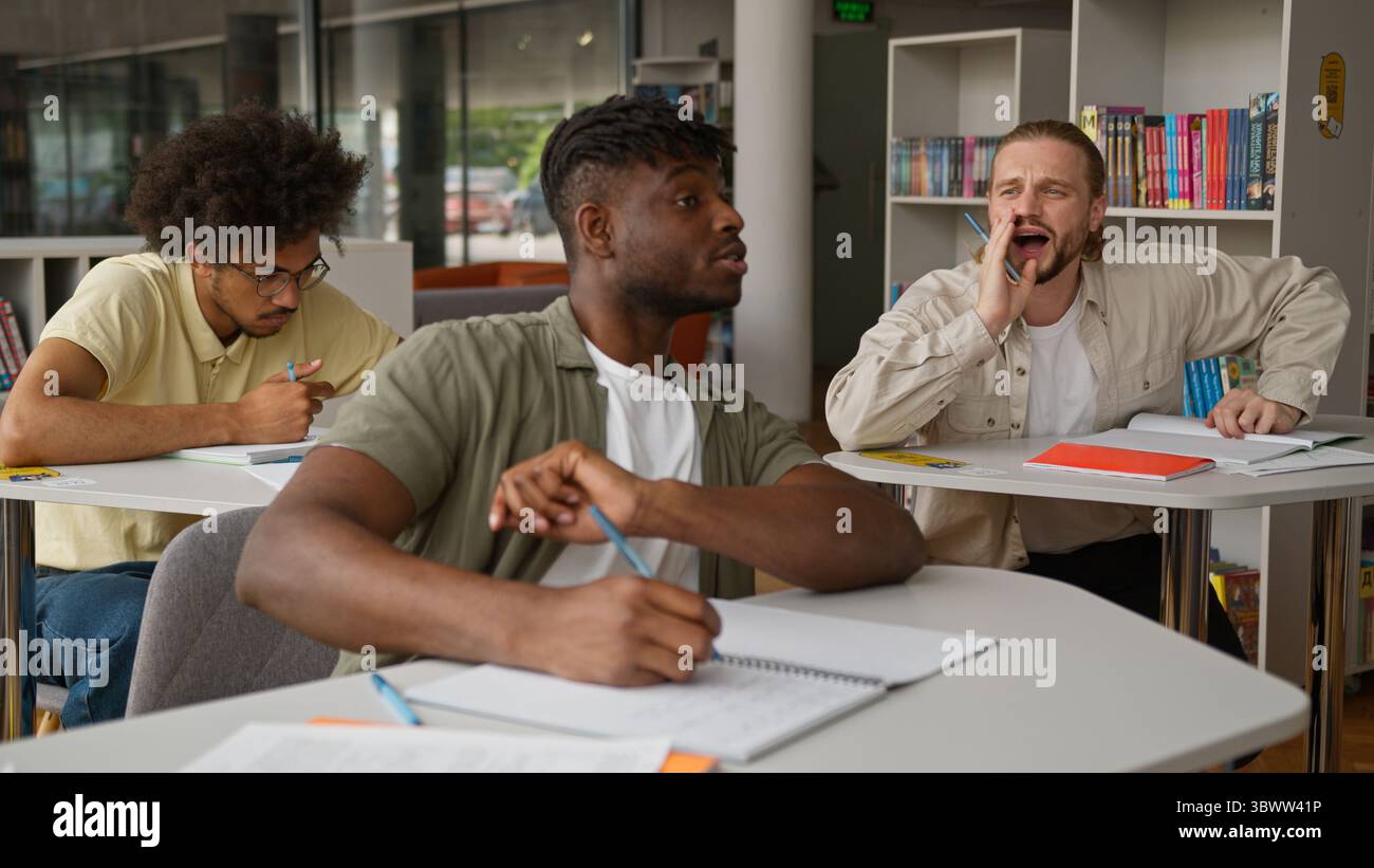 Three multiracial students studying learning in class lesson Caucasian guy asking question study problem talking showing ok diversity men guys writing Stock Photo