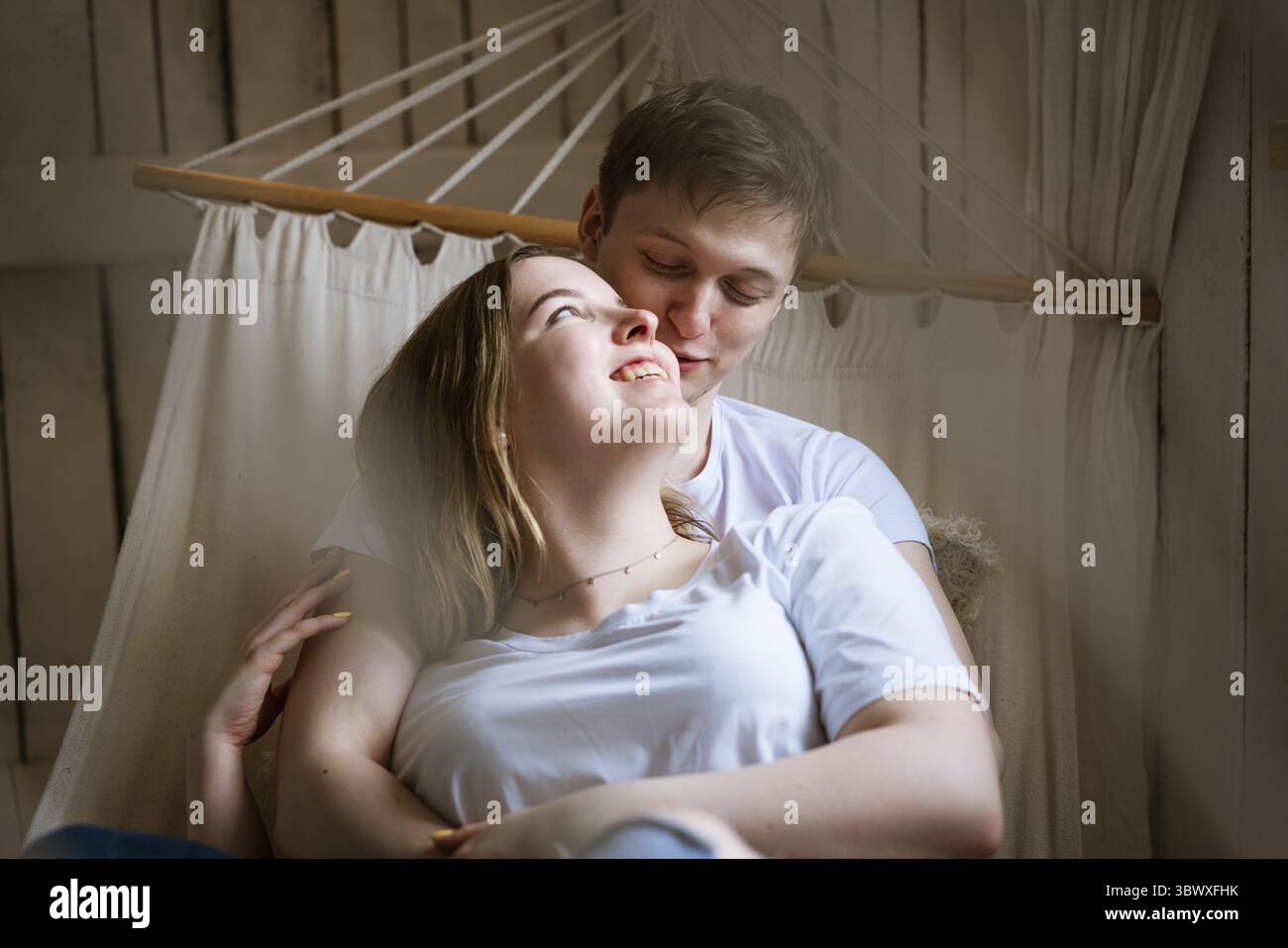 Portrait of a young beautiful couple, a young adult man and a woman in a hammock. the woman is an attractive blonde, the man is dark-haired in a white Stock Photo