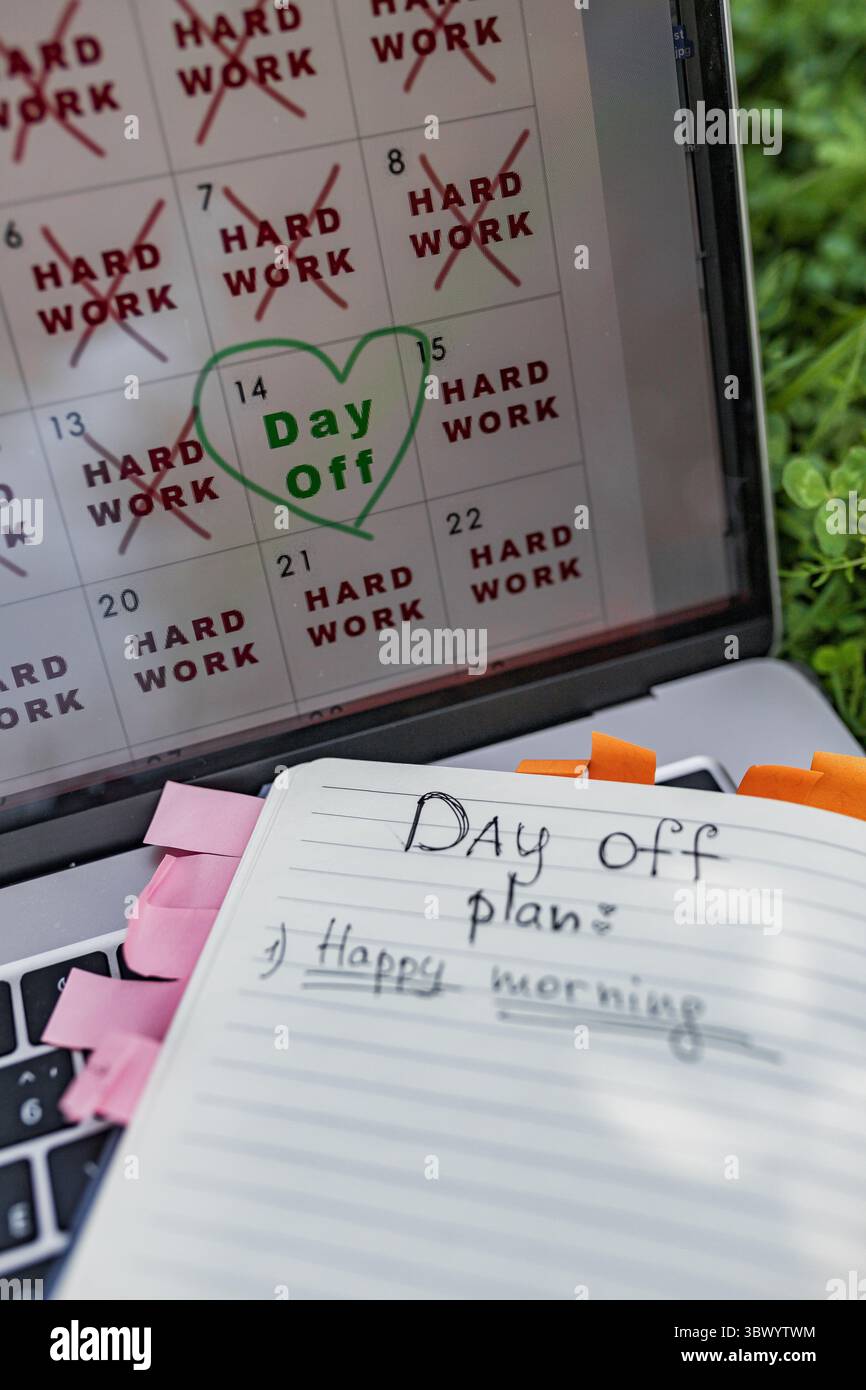 Notebook open with handwritten 'Day Off plan' and laptop showing calendar on green grass. Stock Photo