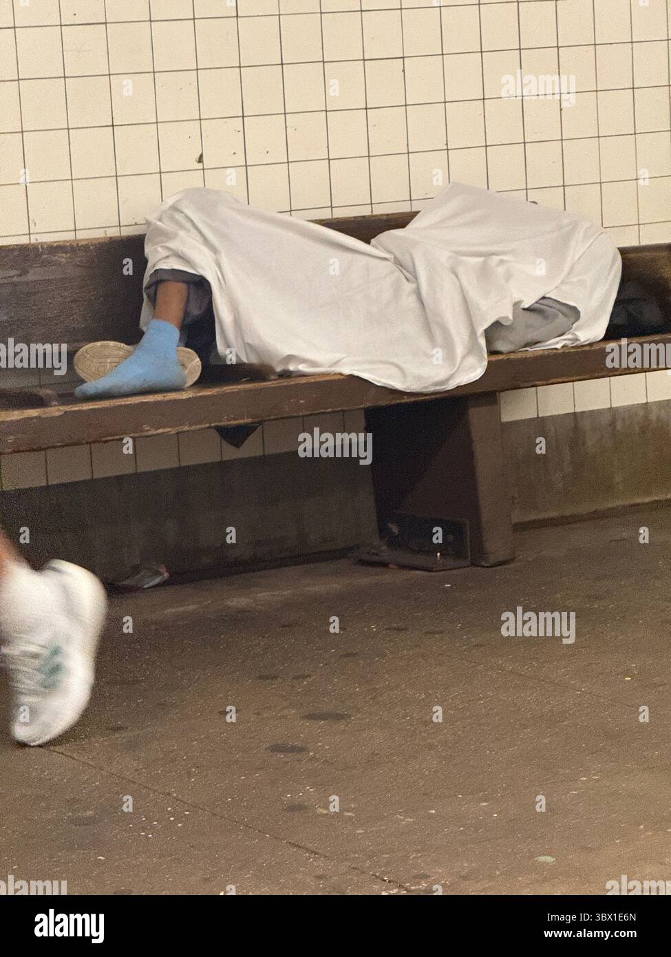 Homeles person sleeps on a bench covered by a sheet on the platform at ...