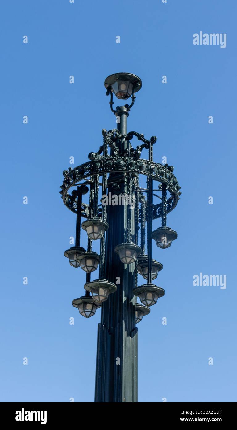 Farola ornamental de estilo clásico en Vigo. Estructura de hierro forjado con múltiples luminarias colgantes, fotografiada contra un cielo azul.España Stock Photo