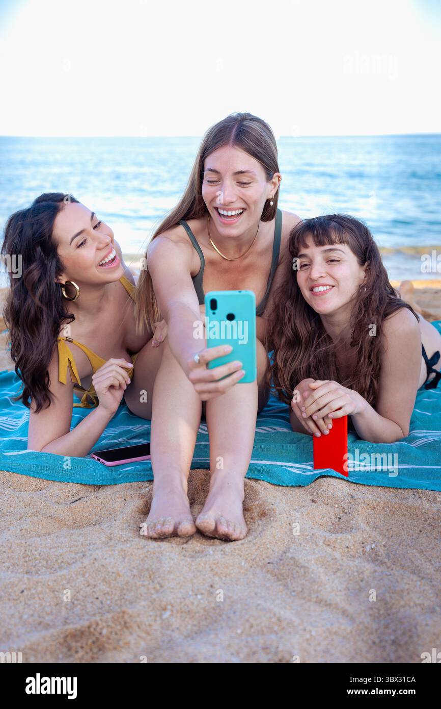 Vertical portrait three young woman using smartphone app on the beach Stock Photo